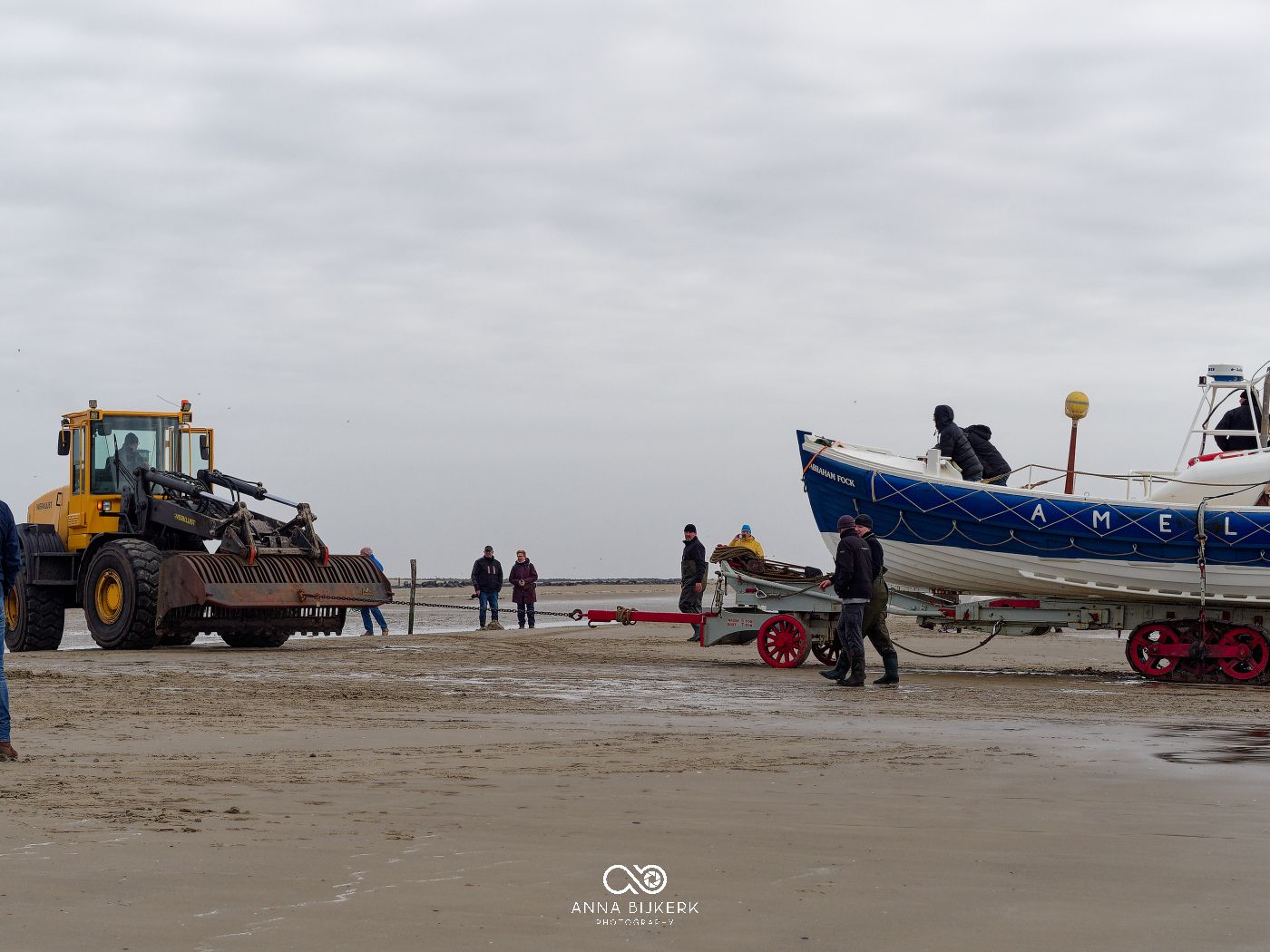 Heavy machinery and vehicles line up along a foggy beach during a winter morning.