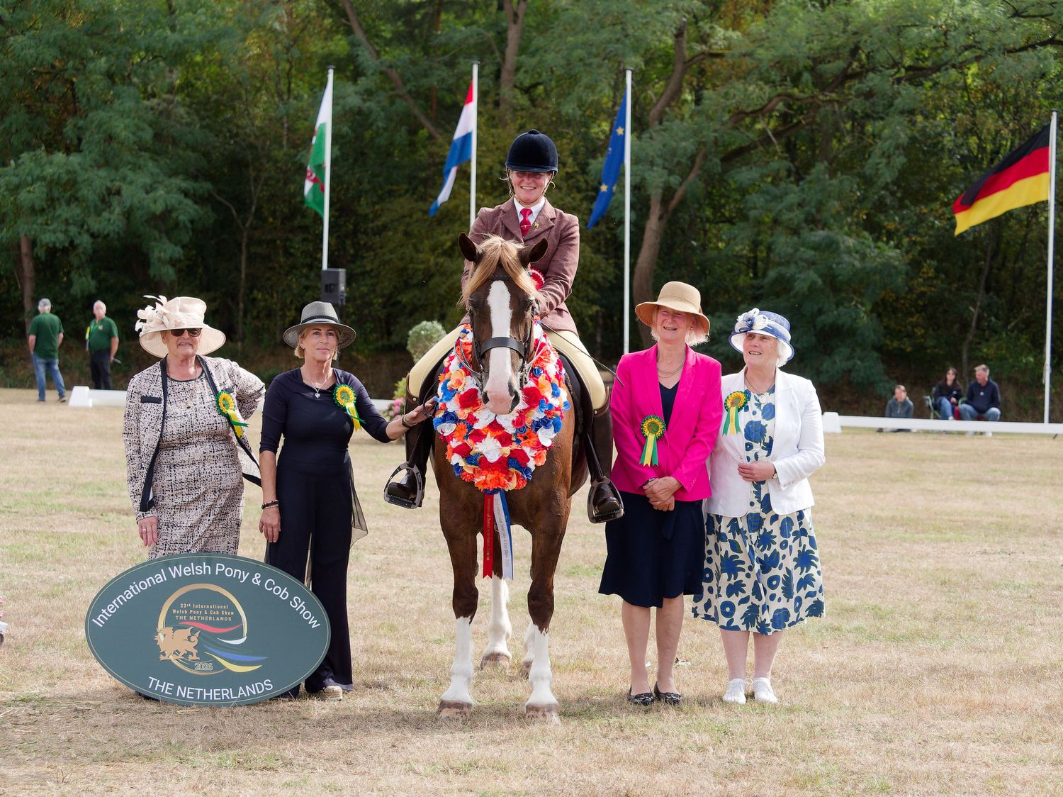 Award ceremony with rider on decorated horse surrounded by women in hats at an equestrian show competition.