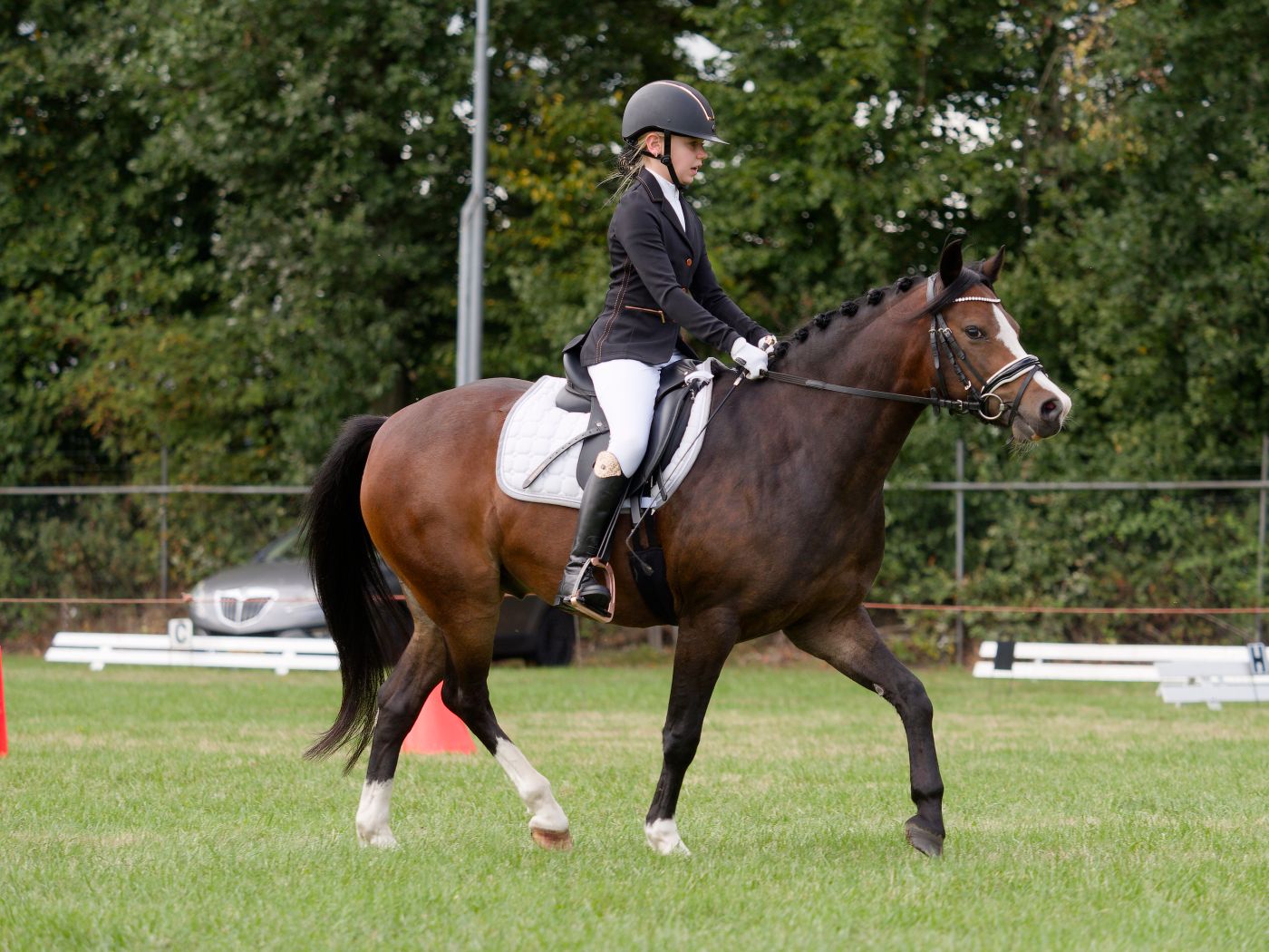Equestrians practice dressage routines on horseback in a fenced outdoor arena.