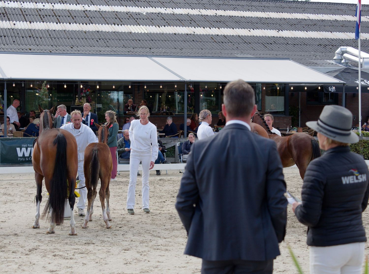 Spectators line the edge of a covered equestrian arena during a horse event.