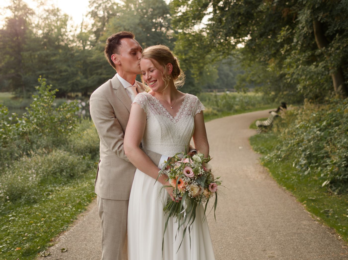 Bride and groom share a romantic moment on a garden path, bride holding a pastel bouquet in golden evening light.