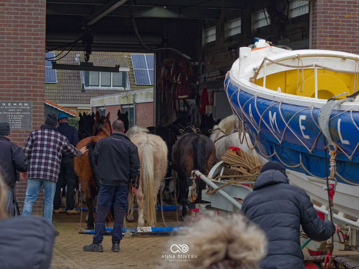 A group of people gather around parked kayaks and canoes outside a brick building.