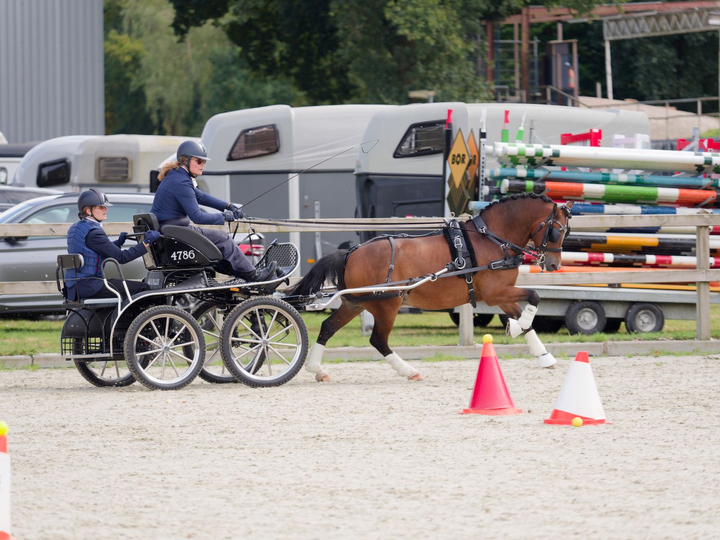 Equestrian carriage driving competition with obstacles set up in a sandy outdoor arena.