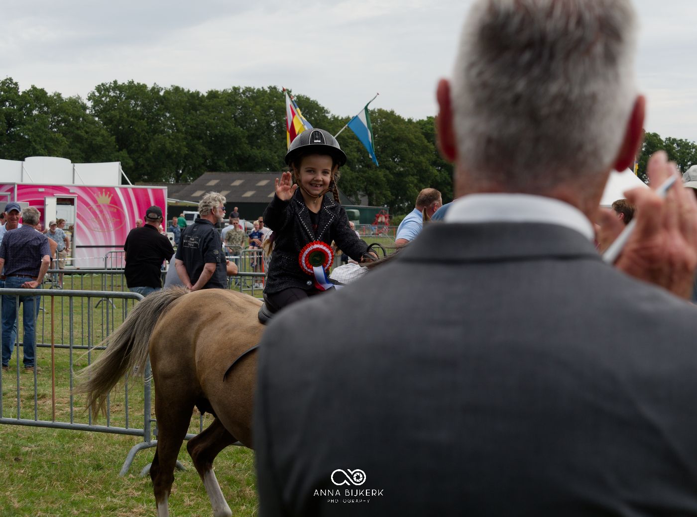 Horses and handlers participating in an outdoor equestrian event with spectators and fencing visible.
