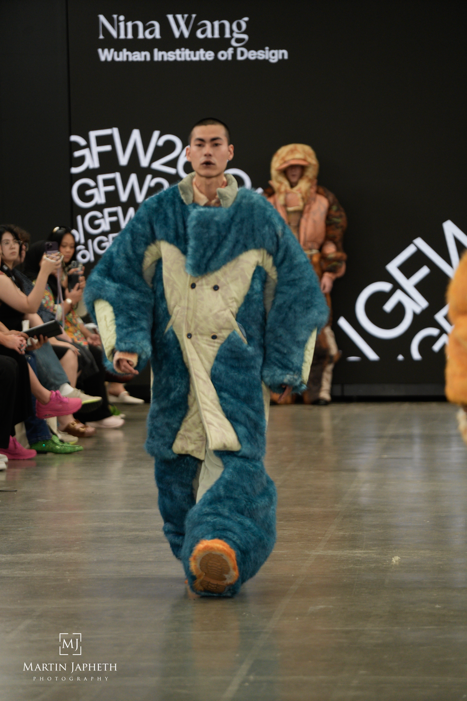 Model walks runway in oversized teal furry coat at Nina Wang Wuhan Institute of Design GFW fashion show. Martin Japheth Photography