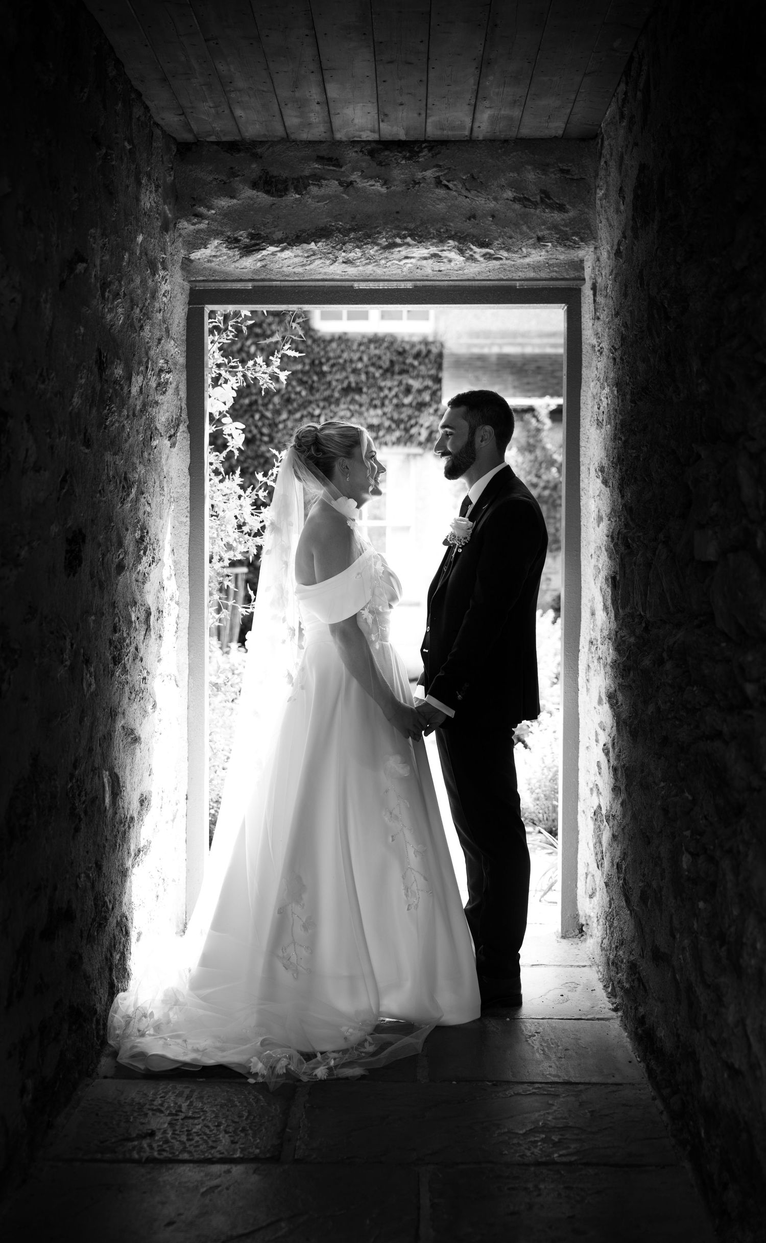 Black and white photo of Yasmin and Tom standing in a stone doorway, facing each other on their wedding day at Plas Cadnant.
