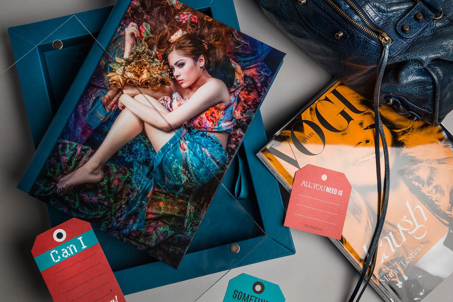 Teal gift boxes with fashion photo print, red tags, Vogue magazine, and denim jeans styled flat lay arrangement.