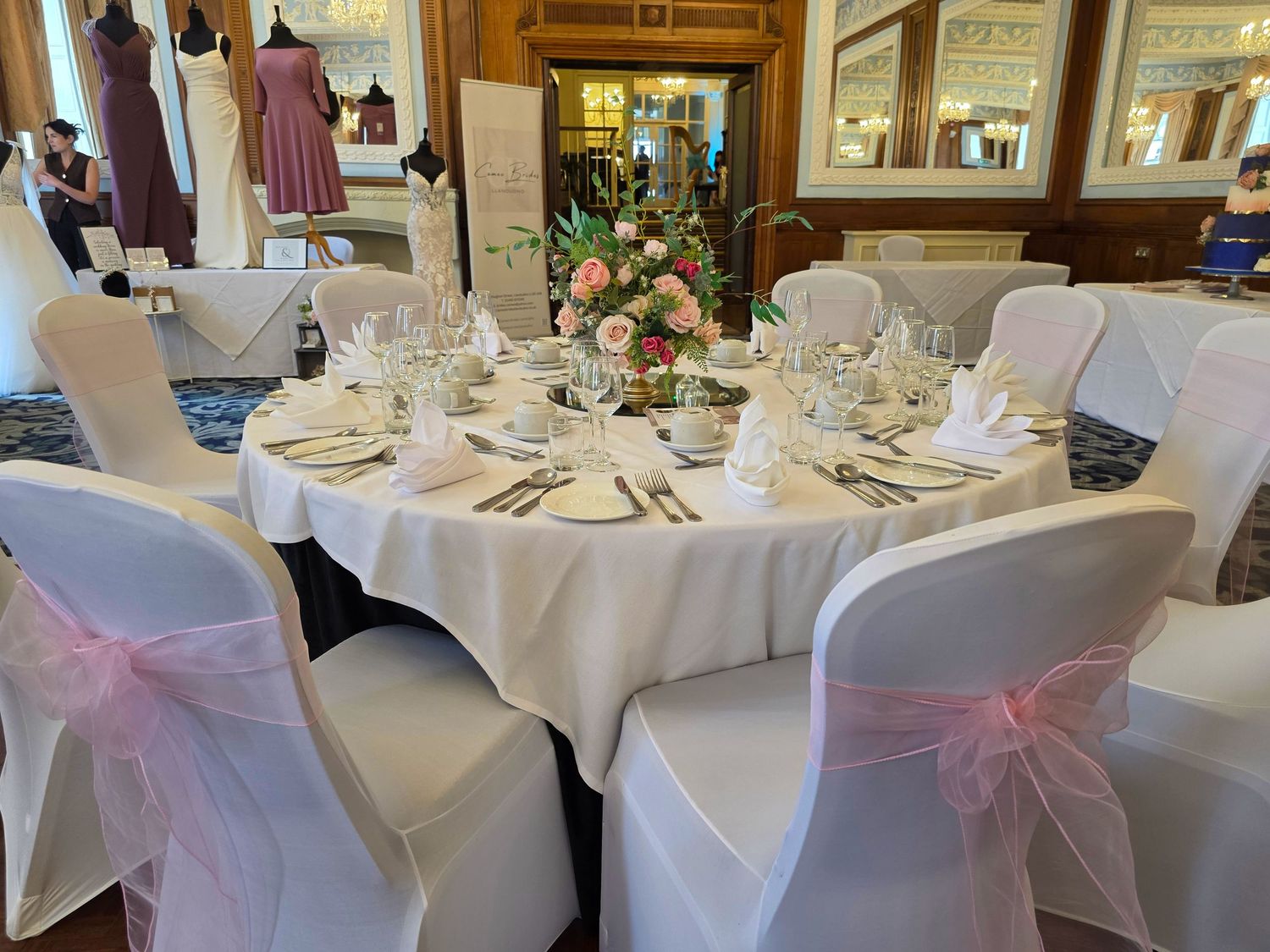 Elegant wedding reception tables with white linens and pink chair sashes in a formal banquet setting. St. George's Hotel Llandudno