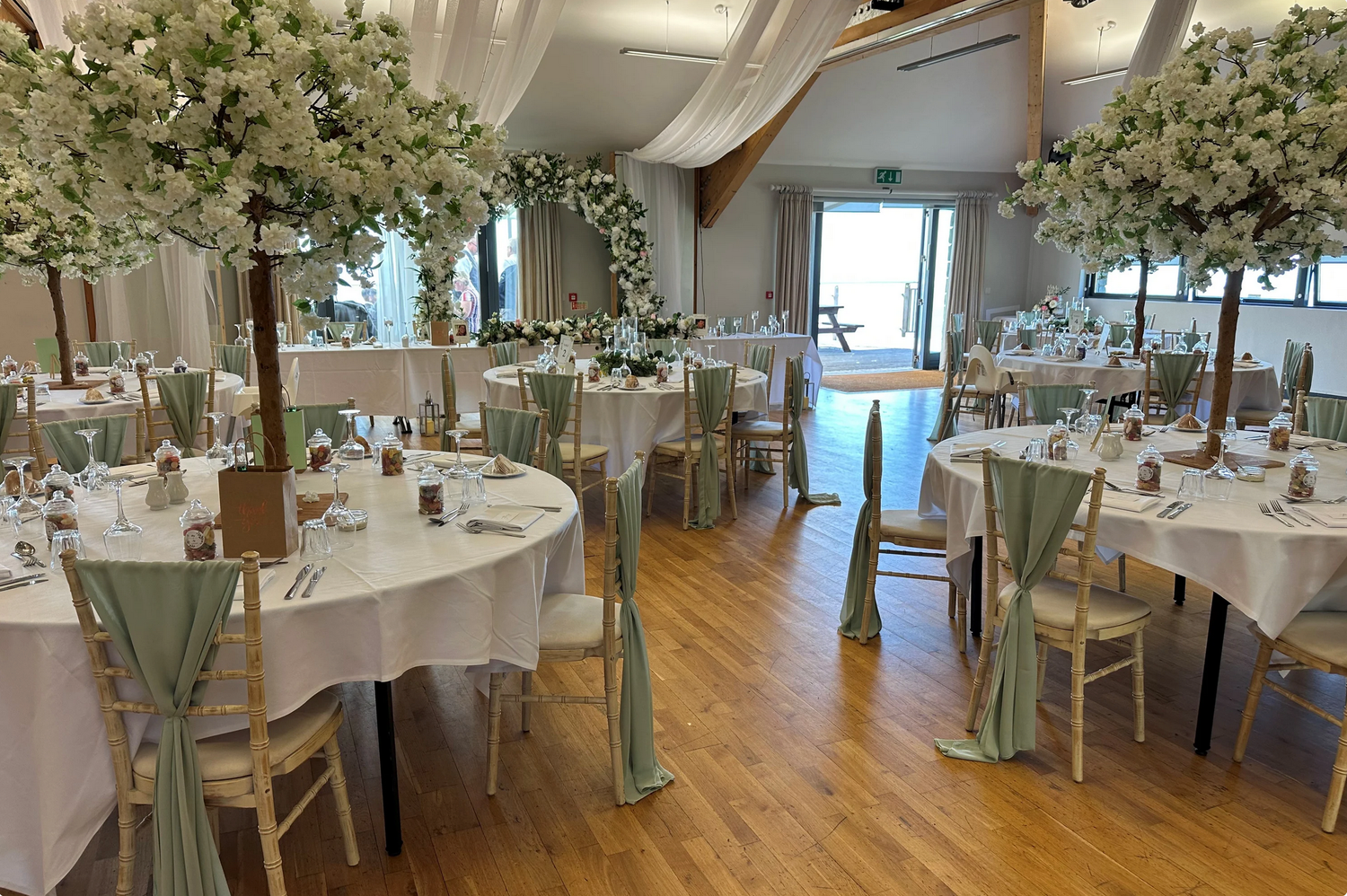 White banquet tables decorated with elegant floral centerpieces and greenery in a bright modern reception venue.