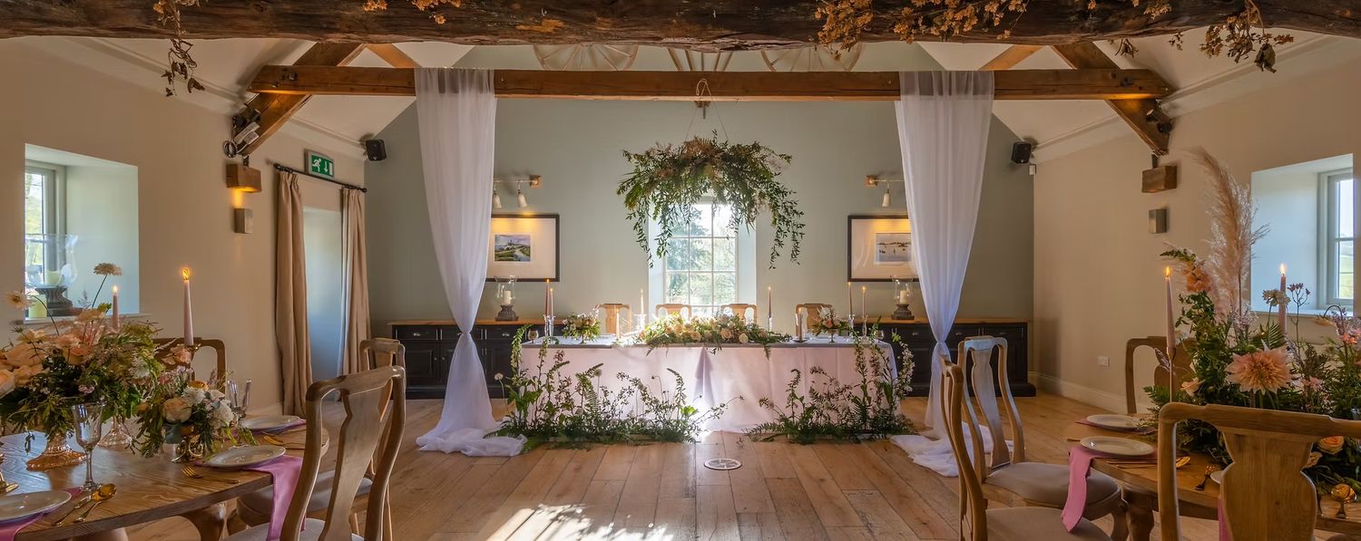 Cozy rustic dining room with exposed wooden beams, pendant lights, and natural decor elements creating a warm atmosphere. Hayloft at Bodnant