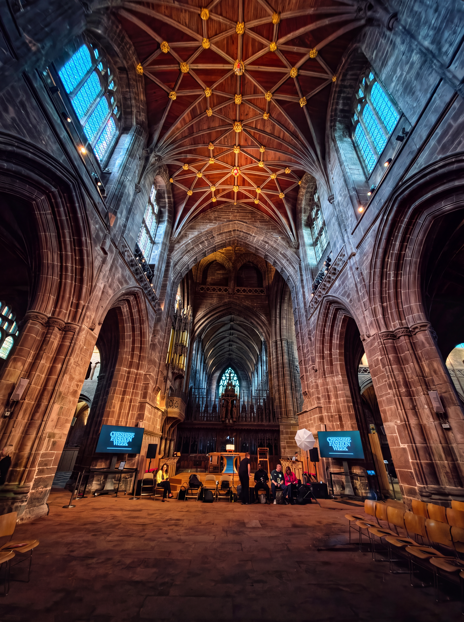 Gothic cathedral interior with ribbed vaulted ceiling, stone arches, and stained glass windows illuminated by dramatic lighting.