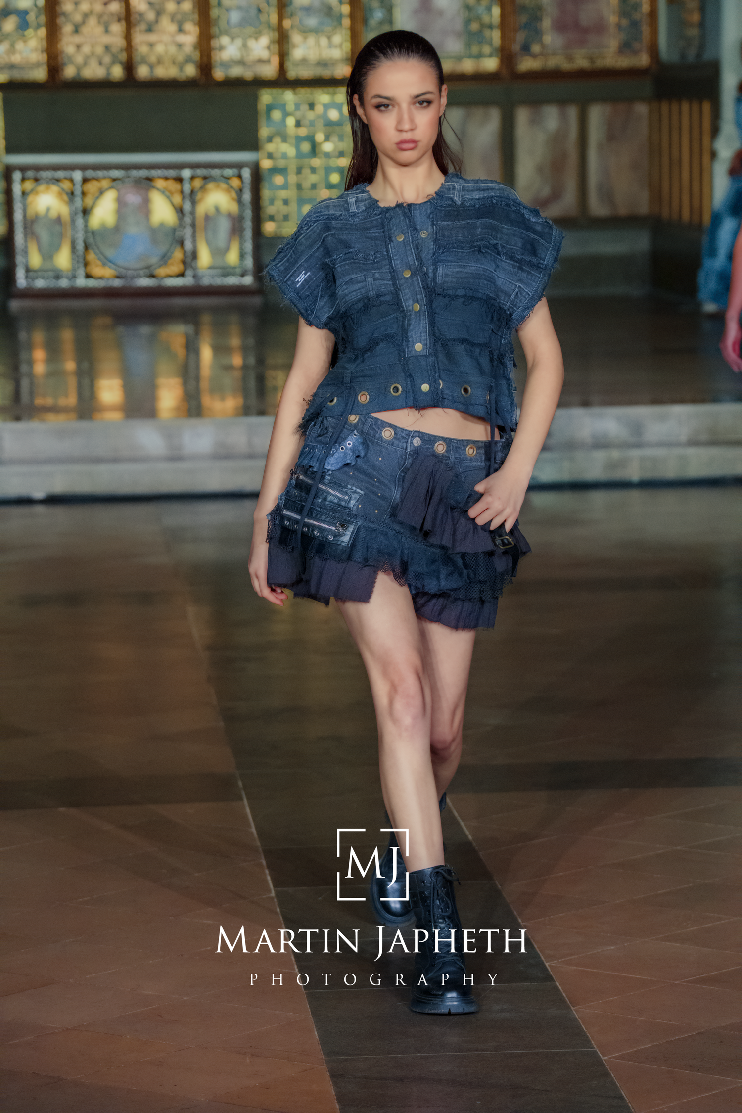 Fashion model in denim crop jacket and shorts poses against industrial backdrop in artistic photoshoot series.