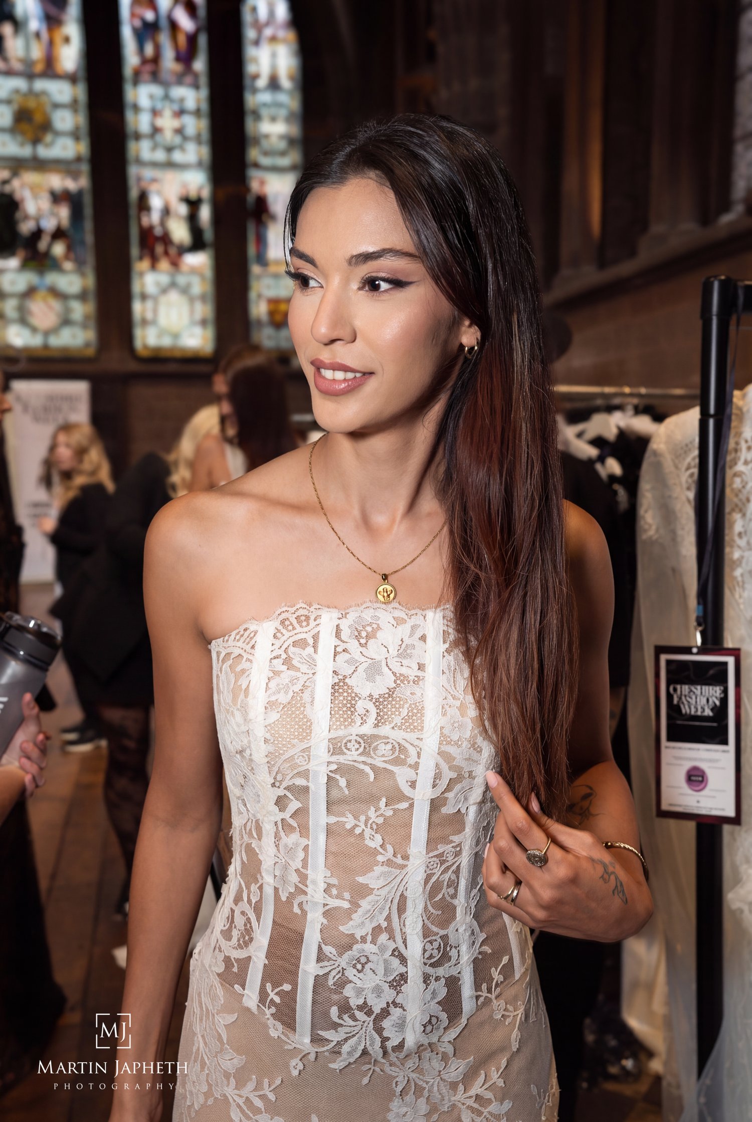 Woman in white lace corset gown at a fashion event inside an elegant venue with stained glass windows.