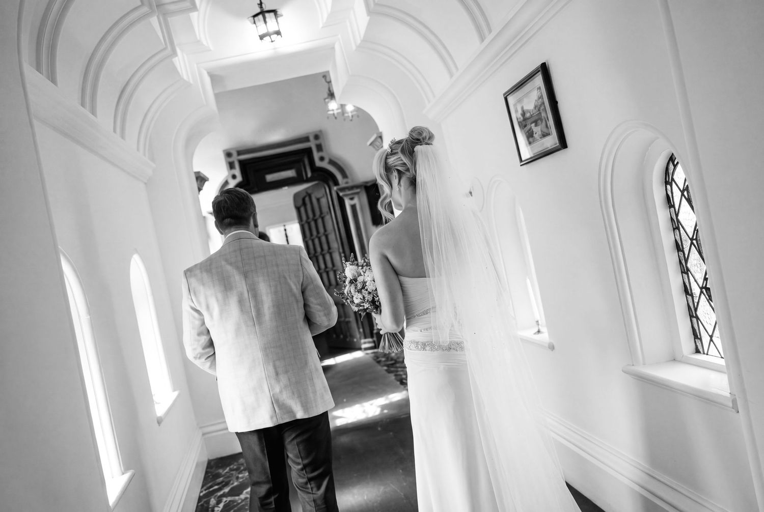Black and white photo of a bride and groom walking down the reception hallway on their wedding day at Chateau Rhianfa Wedding