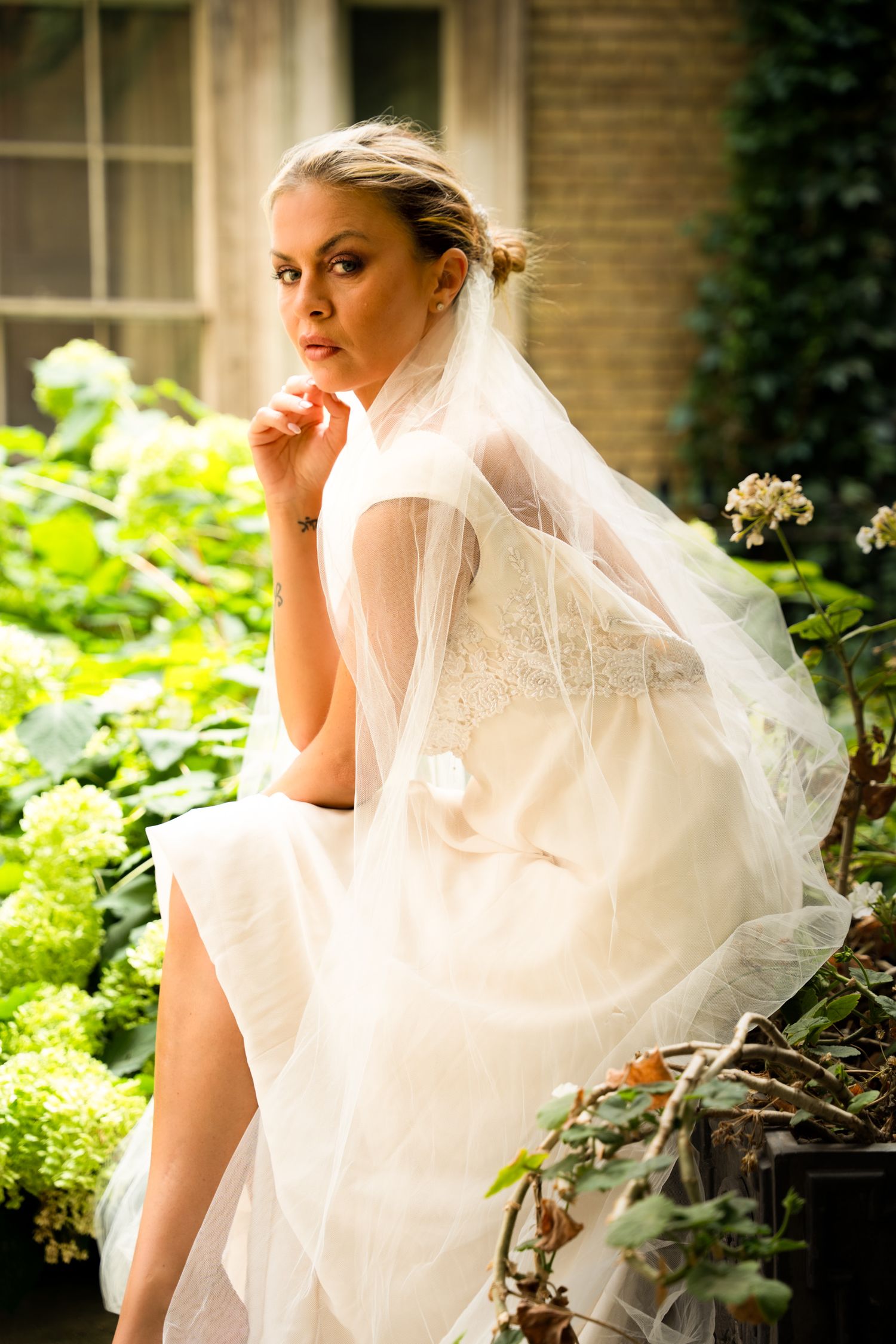 Bride seated among green hydrangeas in the garden at the Church of St Magnus the Martyr, London