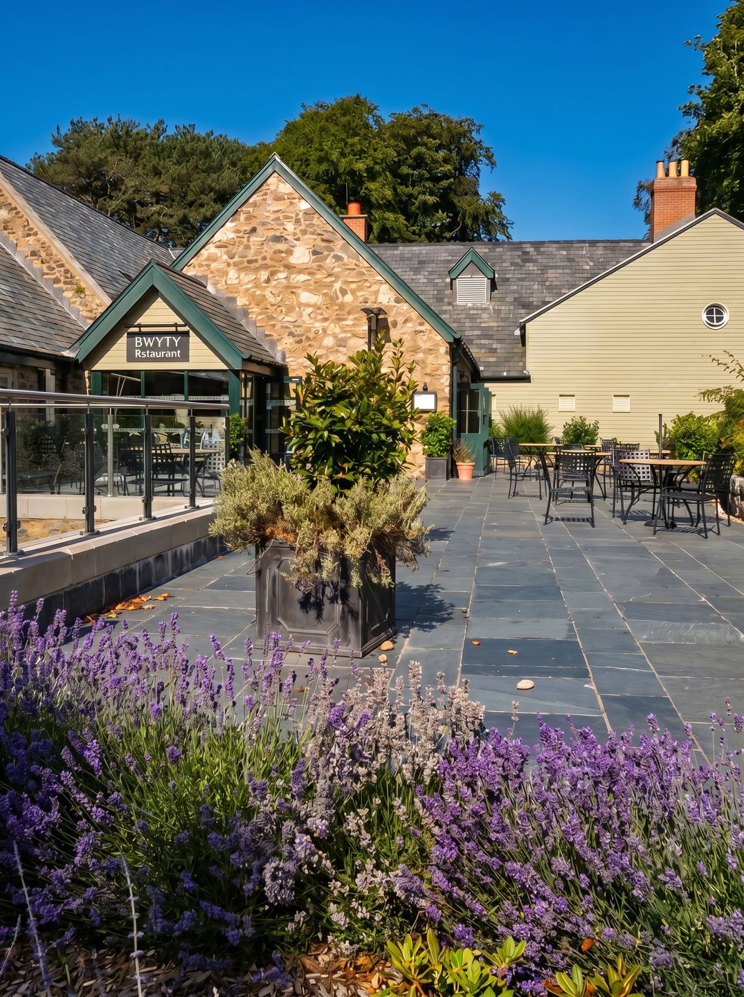 Stone and timber restaurant exterior with lavender garden, outdoor dining terrace, and blue sky in a charming heritage setting.