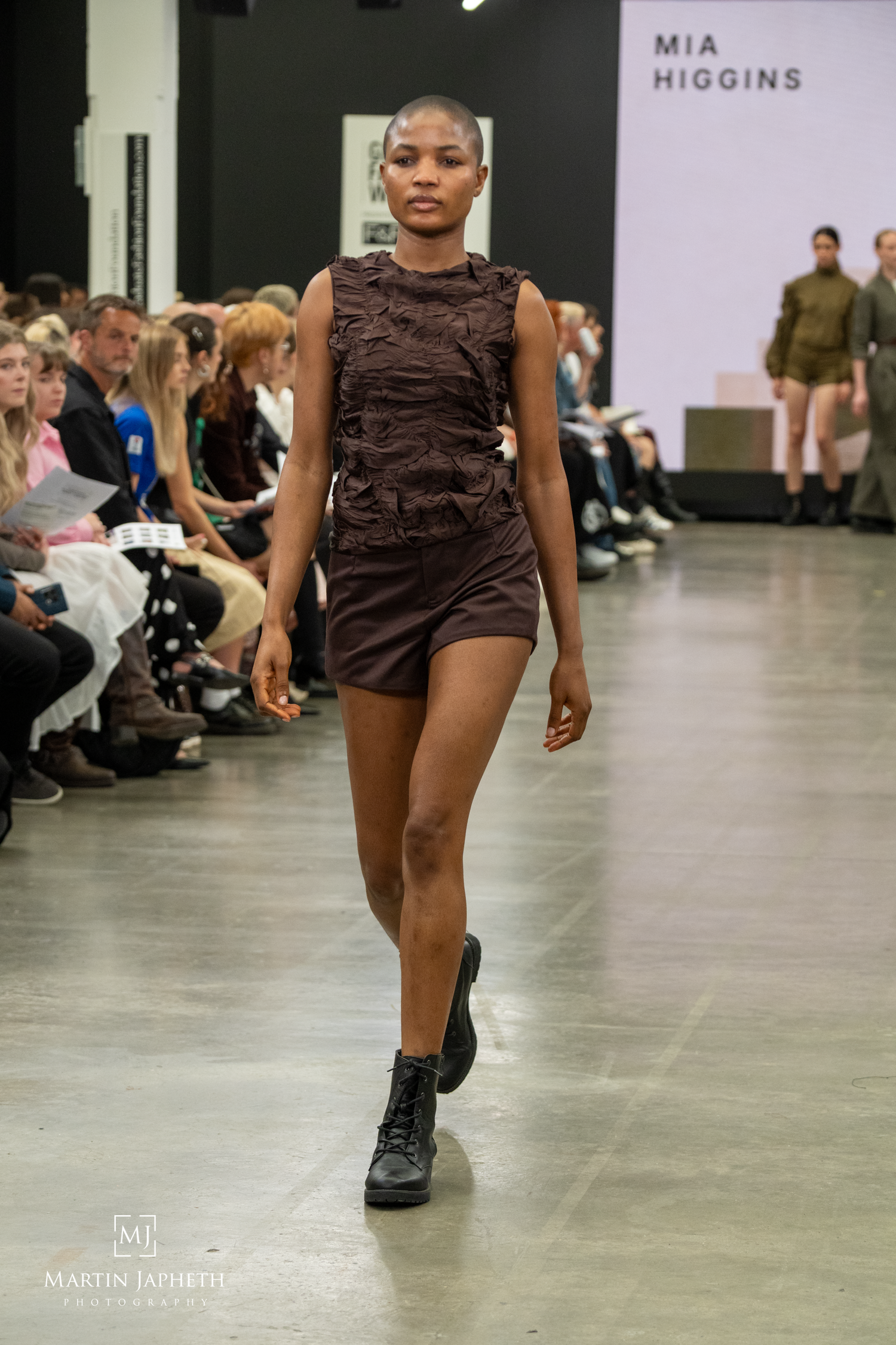 Model walks runway in brown textured mini dress and black boots at Mia Higgins fashion show.Martin Japheth Photography