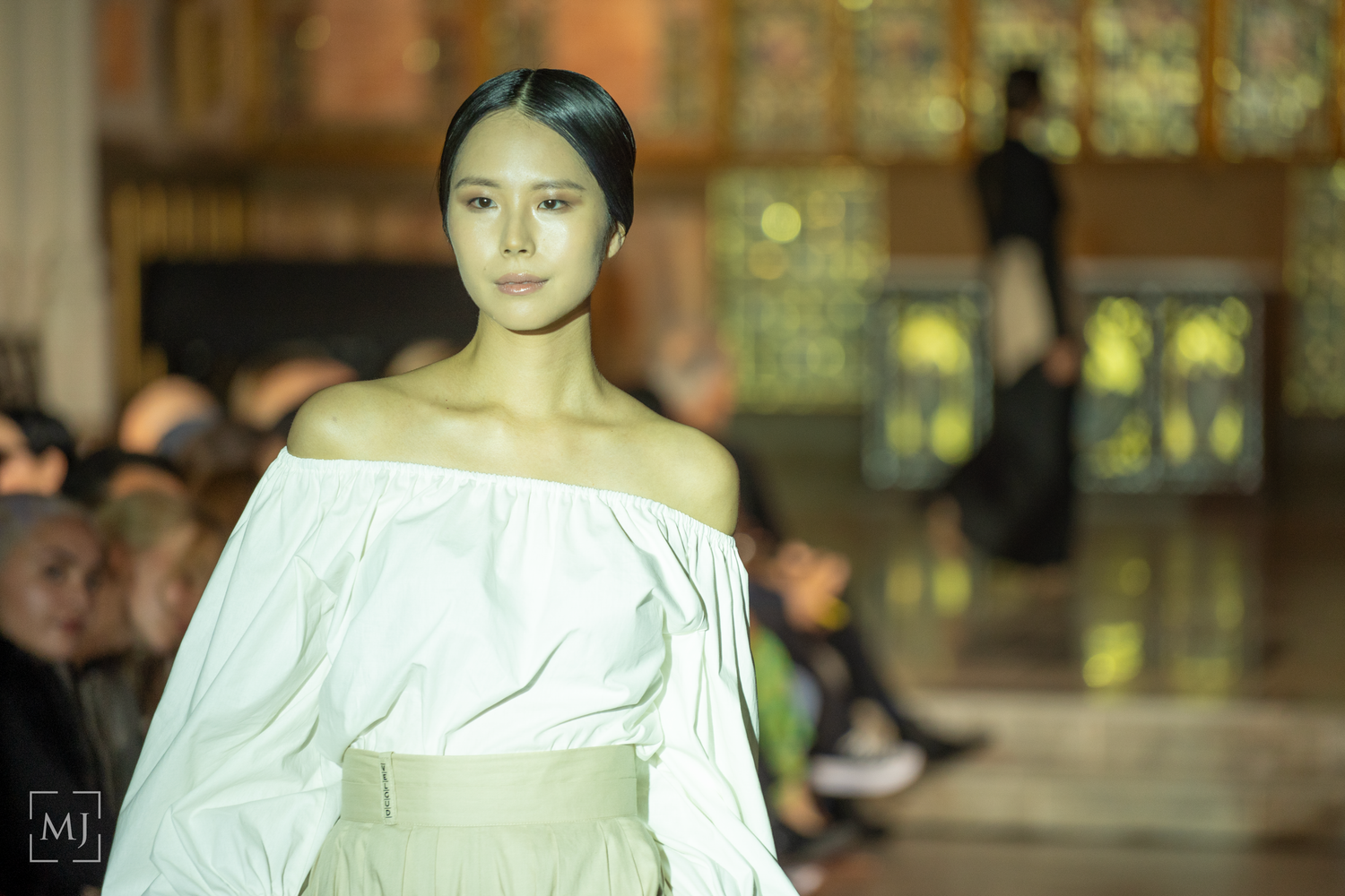 Models walk the runway in white off-shoulder dresses during a fashion show presentation.