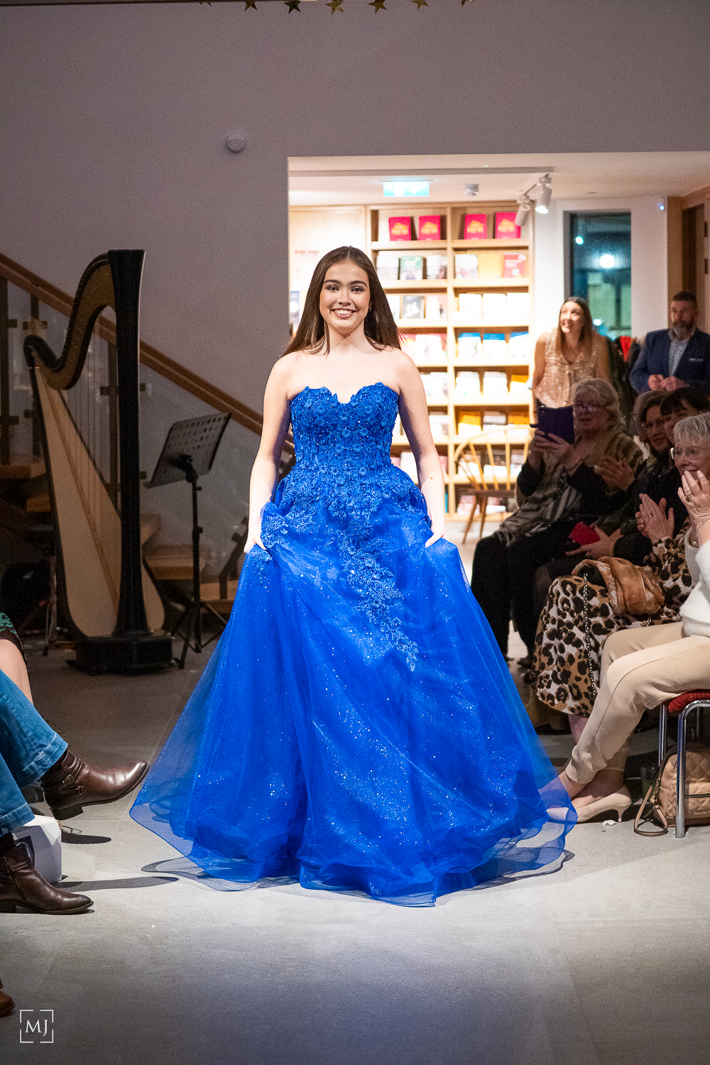A model walks the runway in a stunning royal blue ball gown with sequins and strapless bodice at a fashion show.