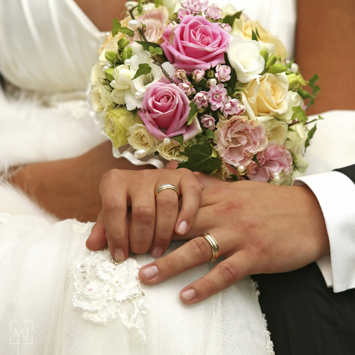 Close-up of wedding rings and hands with pink and white floral bouquet.