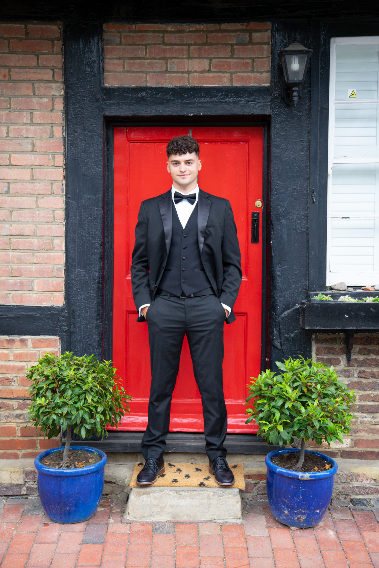 A sequence of four photos showing someone in a formal black tuxedo standing in front of red doors and brick walls.