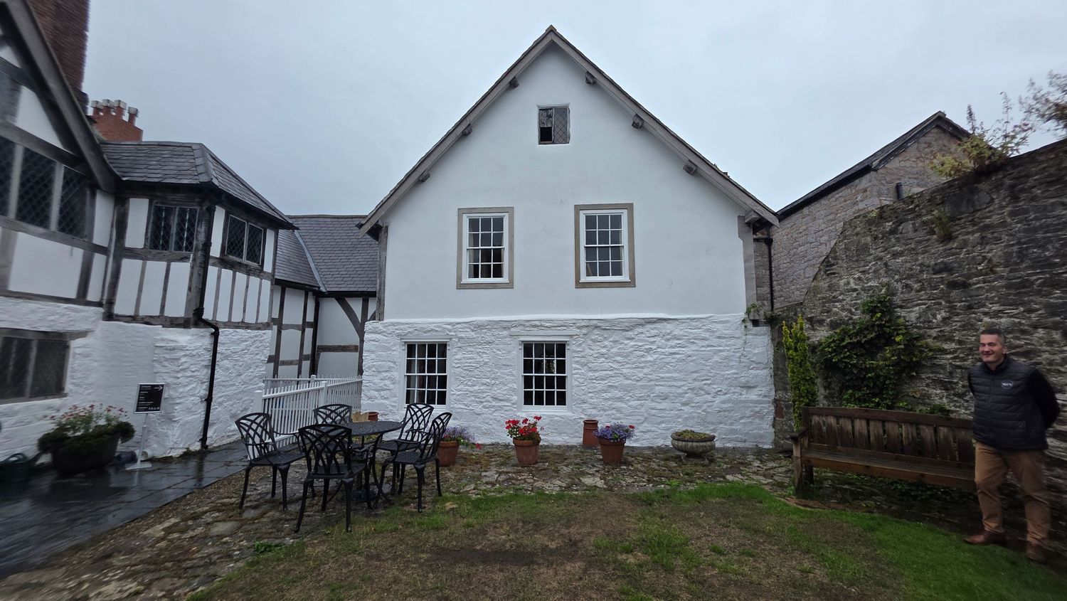 White-painted stone cottage with sash windows, outdoor garden furniture, and a man standing beside a stone wall.
