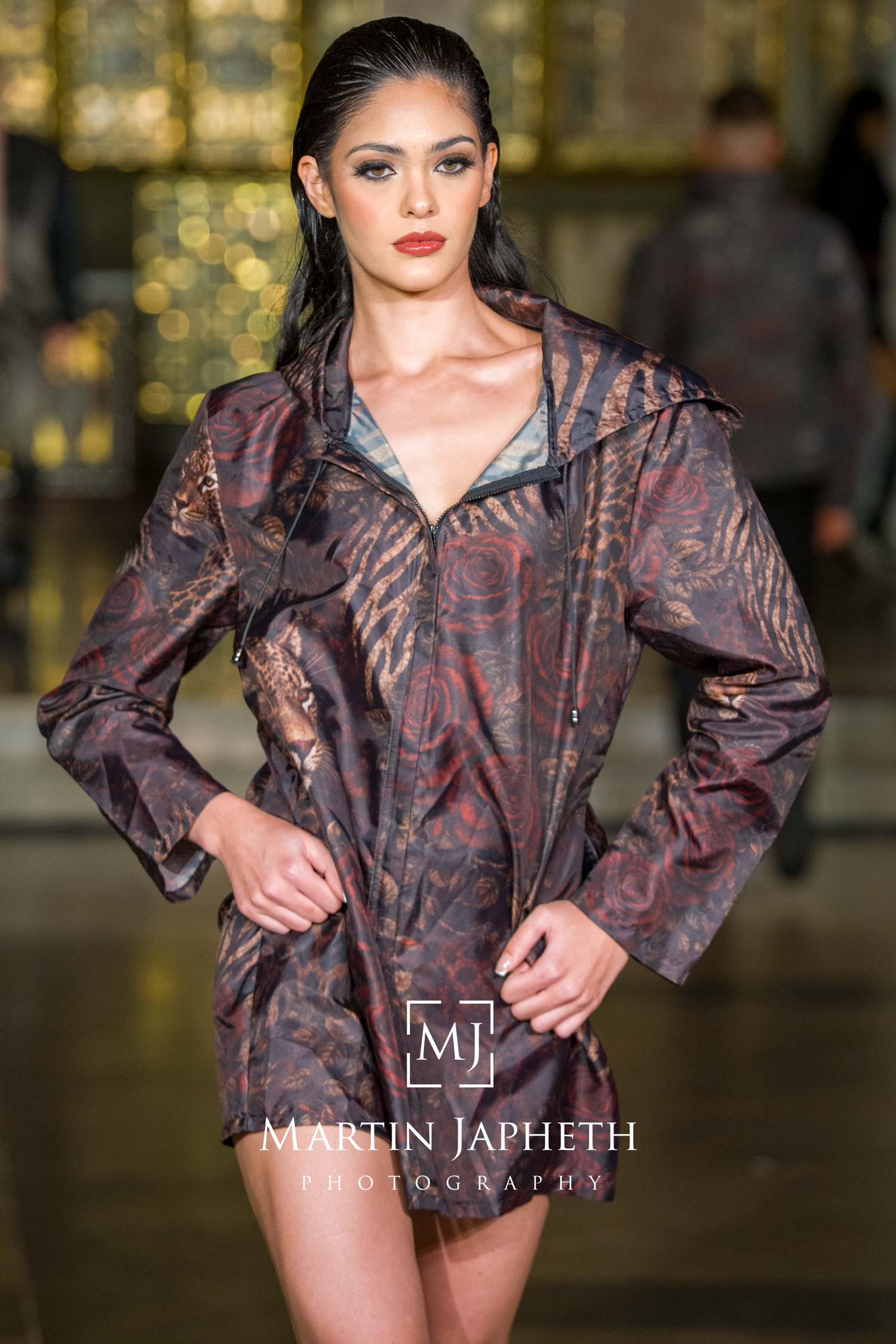 Fashion model wearing a metallic brown ruffled jacket poses on runway in dramatic lighting.