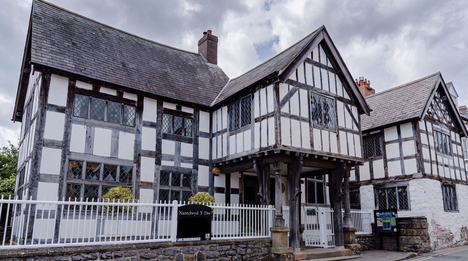 Historic Tudor-style black and white timber-framed manor house with decorative woodwork and traditional architecture.
