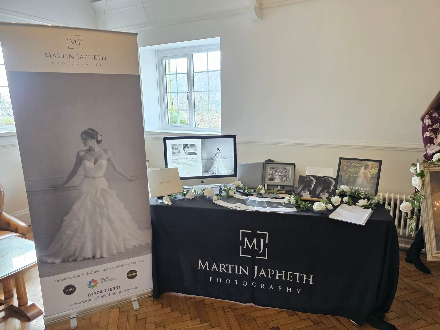 Elegant wedding photography display setup with black tablecloth and branded signage in a bright indoor venue.