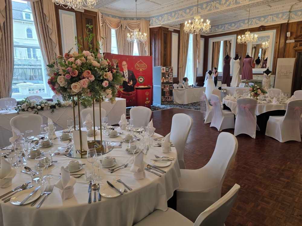 Elegant wedding reception venue with white-clothed tables, floral centerpieces and ornate architectural details.  St. George's Hotel Llandud