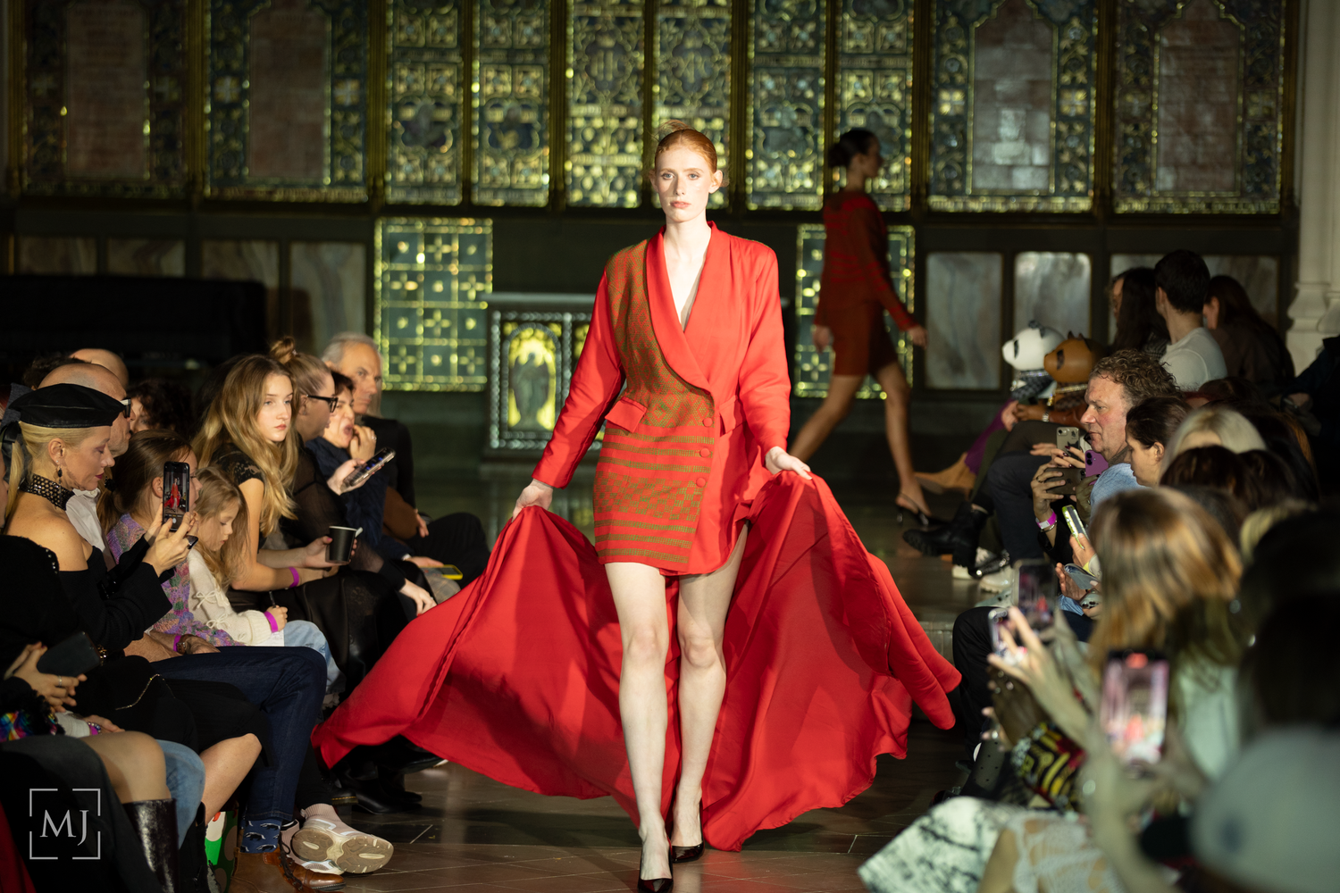 Models walk the runway in dramatic red and white evening gowns at a high-end fashion show.