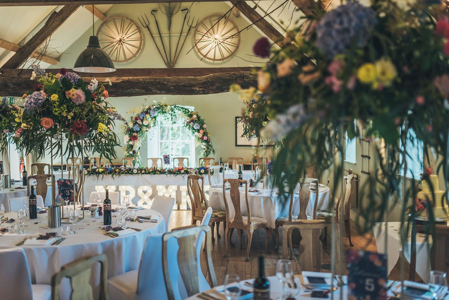 Elegant wedding reception venue with round tables, white linens, floral arrangements and decorative arched windows. Hayloft at Bodnant Foods