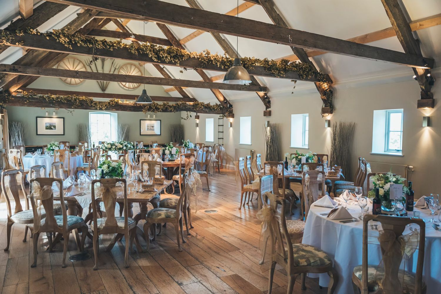 Rustic wedding reception venue with exposed wooden beams and elegant white table settings in a converted barn space. Hayloft at Bodnant Food