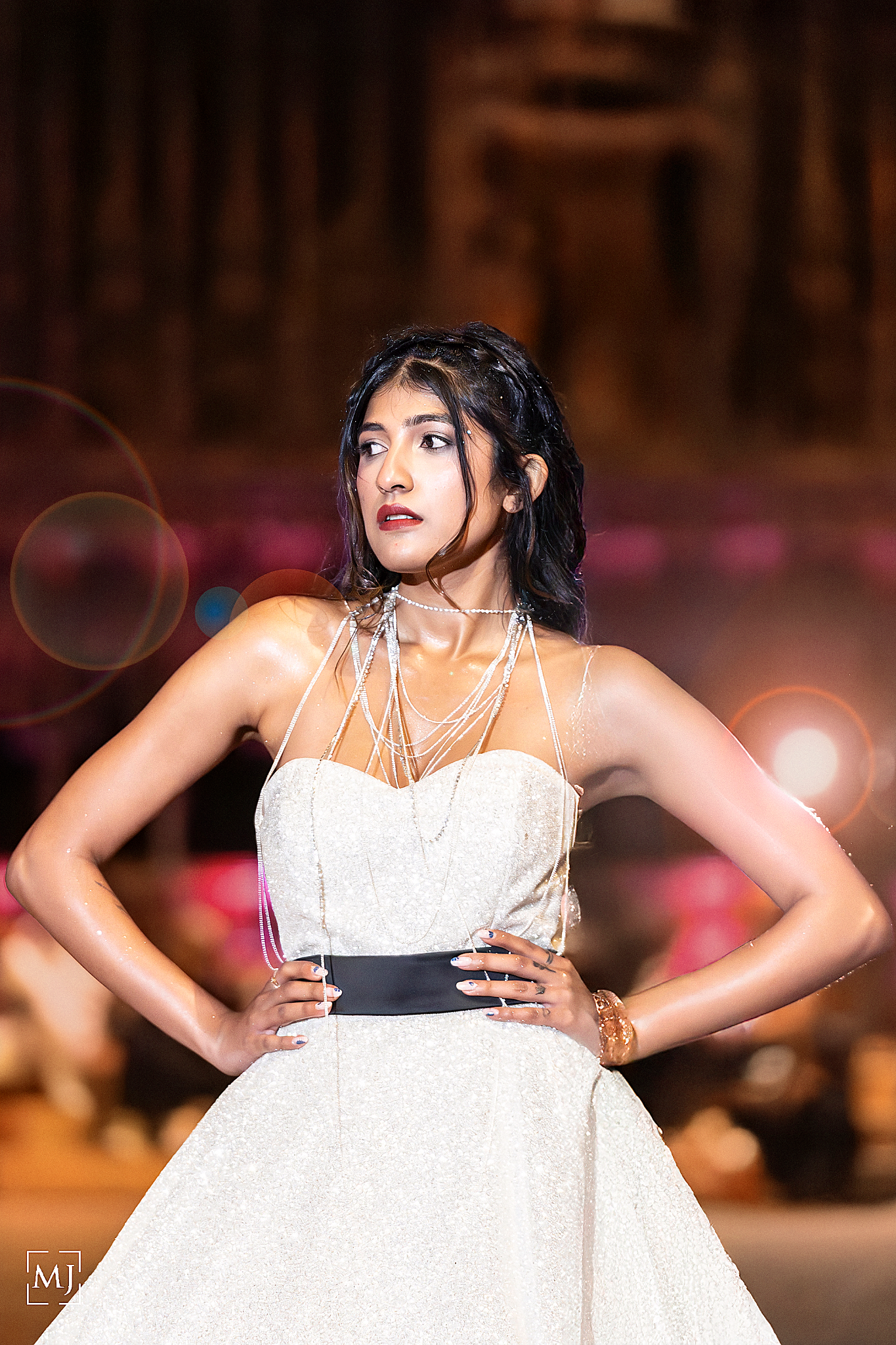 Model in white strapless gown strikes elegant poses during fashion show with warm lighting and blurred background. Fashion Photographer