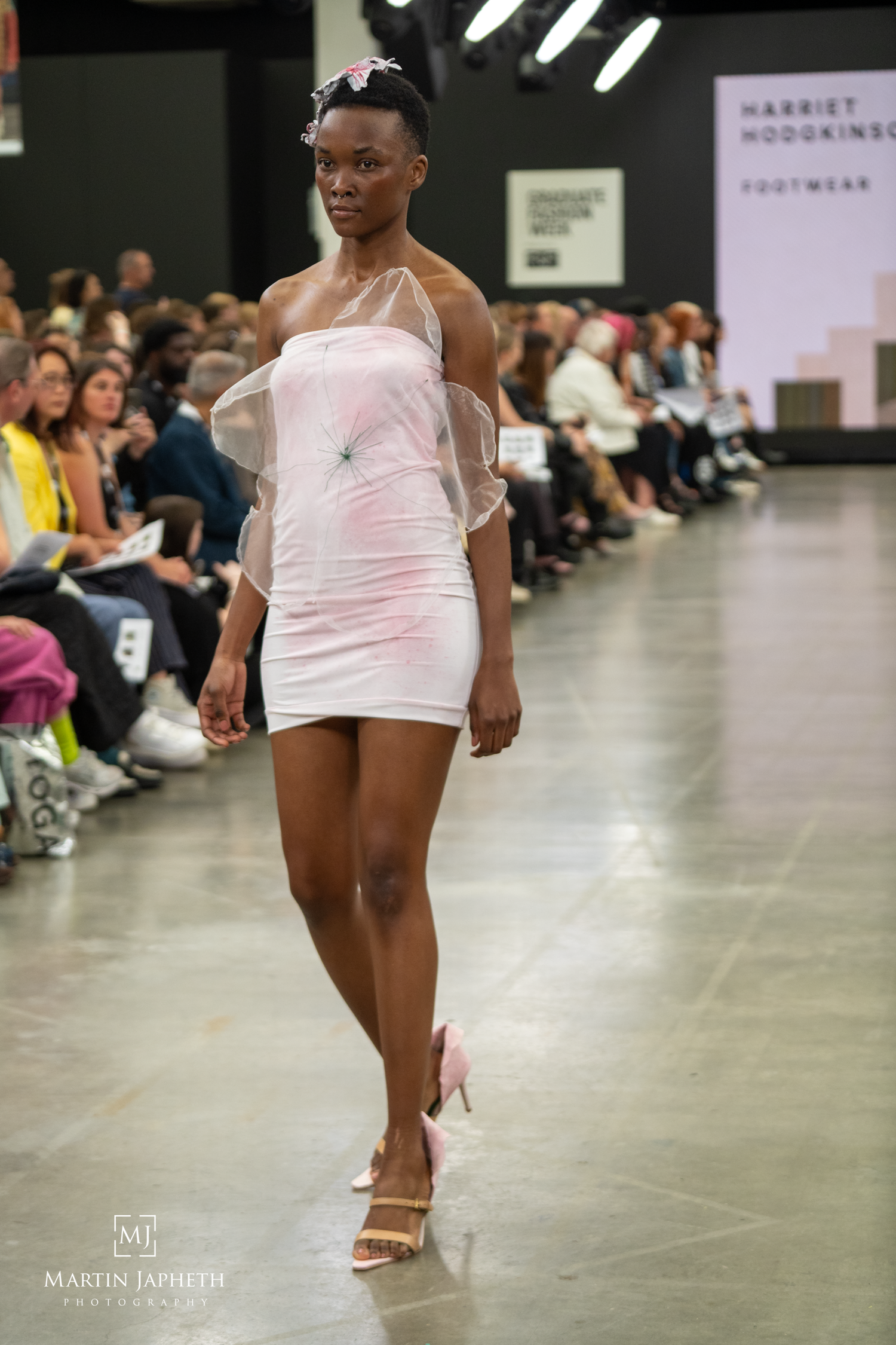 Model walks runway in pink mini dress with sheer overlay at Harriet Hodgkins Footwear fashion show. Martin Japheth Photography