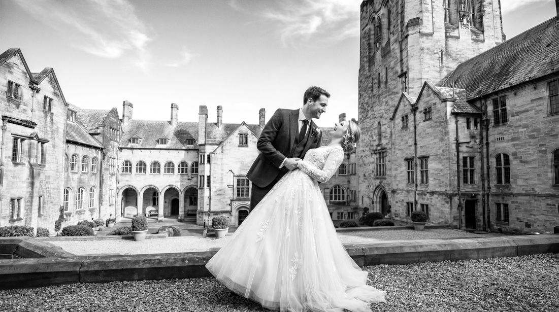 Black and white wedding photo of bride and groom embracing outside a historic stone manor house.