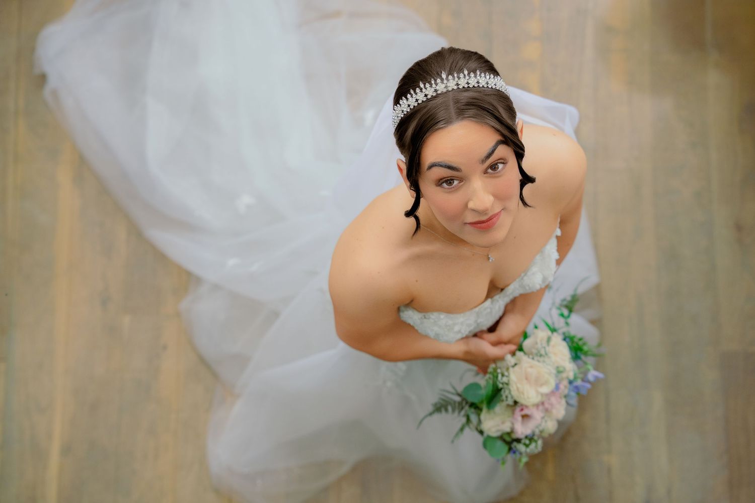 Overhead view of a smiling bride in a white strapless gown and tiara holding a bouquet at Nant Gwrtheyrn.