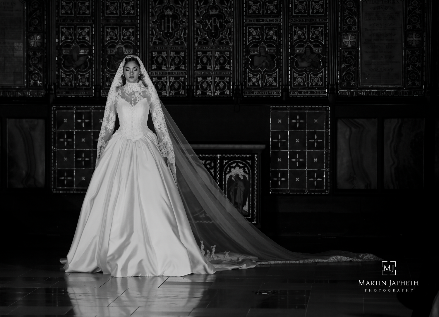 Elegant bridal portrait in cathedral with dramatic veil and ornate gothic architecture.
