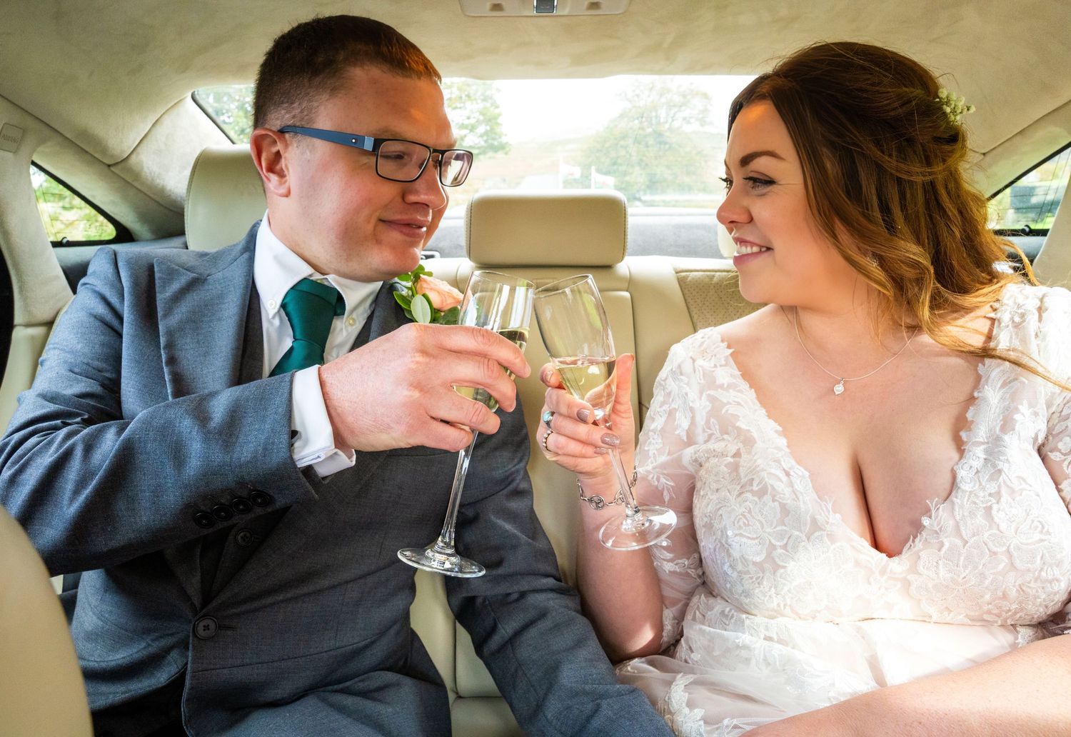 Bride and groom toasting with champagne glasses in a wedding car, smiling joyfully on their special day.