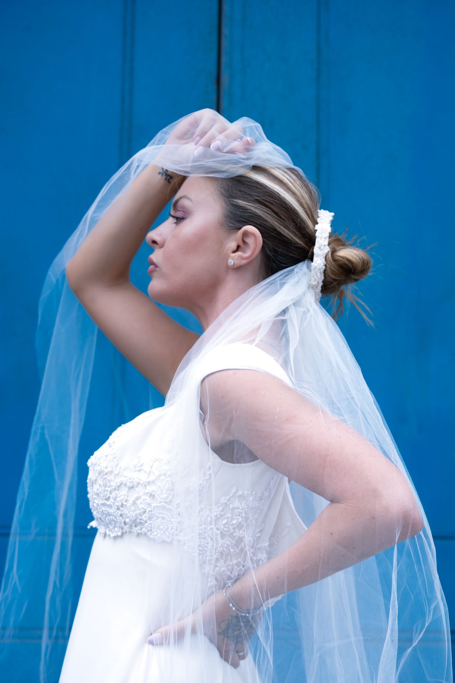 Bride in profile raising her veil against a bright blue door on Tower Bridge Road, London editorial bridal portrait
