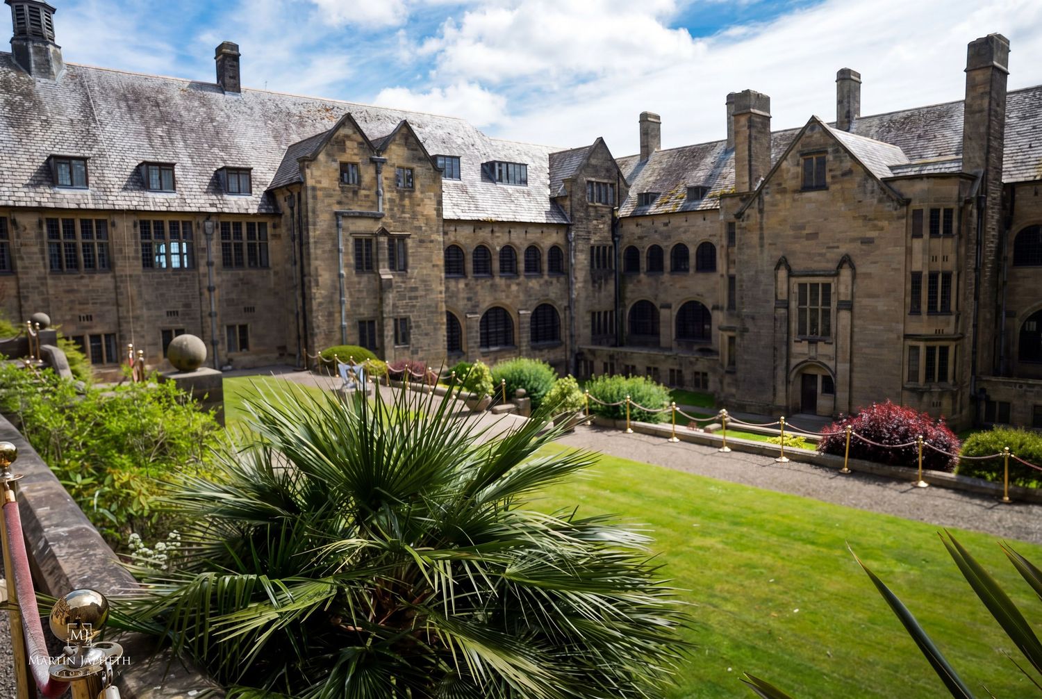 The Quad at Bangor University with manicured lawn, palm tree, and Gothic arched cloisters under a blue sky. Martin Japheth Photography