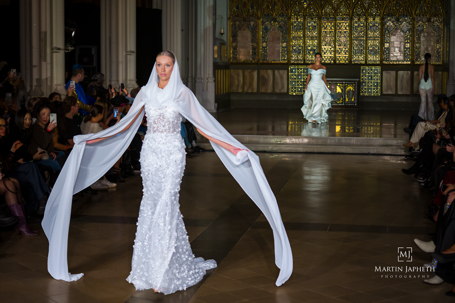 A bride in a lace wedding dress walks through an ornate church with dramatic lighting and architecture.