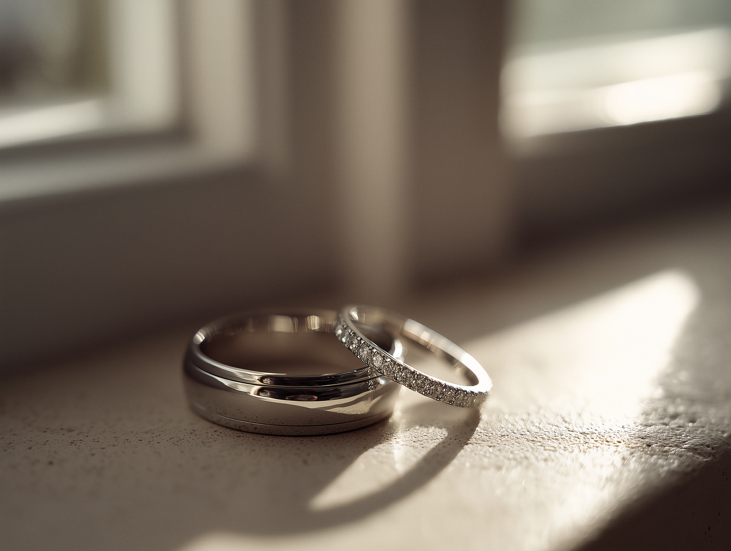 Two gold wedding rings rest on a reflective surface with dramatic lighting and shadows.