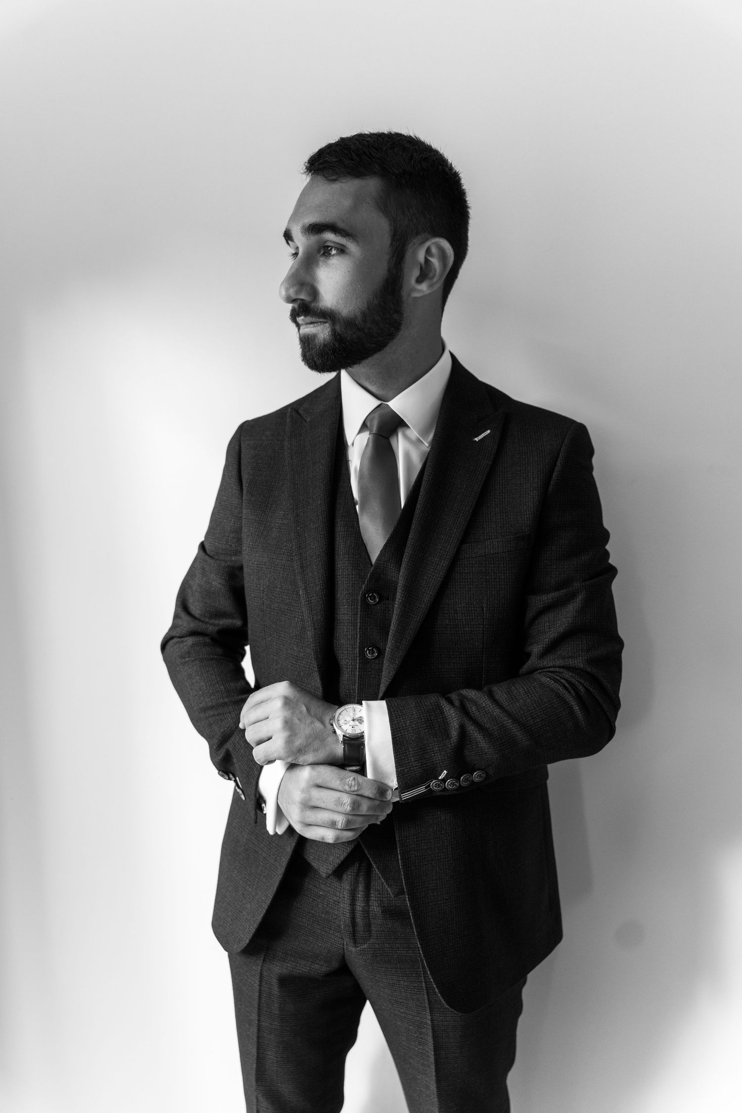 Black and white portrait of Tom in his three-piece suit adjusting his cufflinks against a white background.