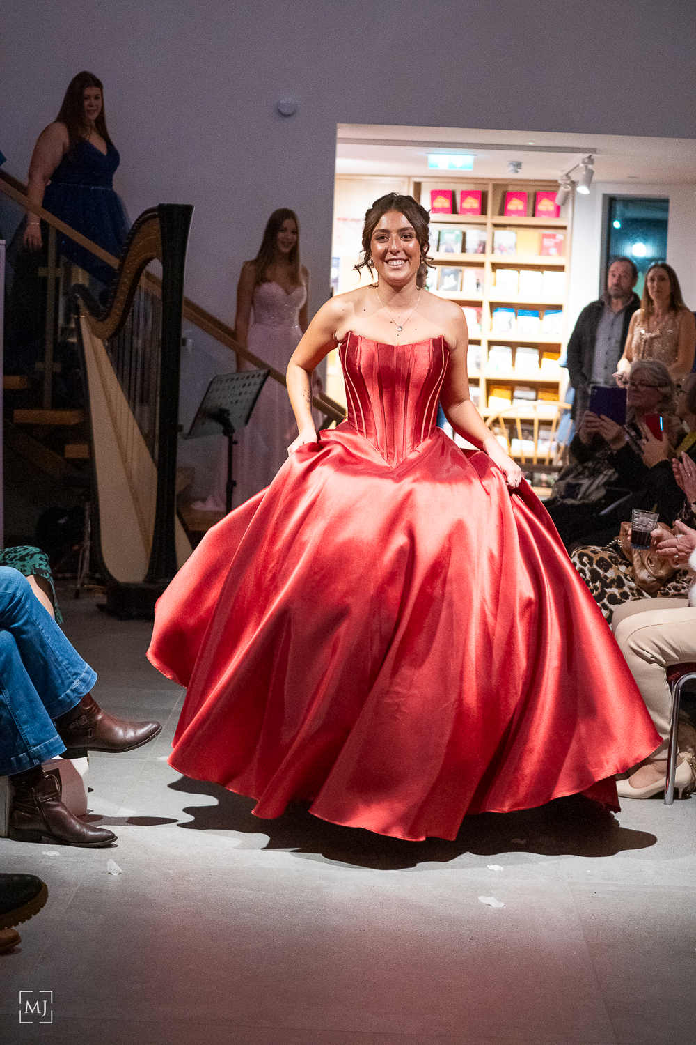 A stunning red satin ball gown with a voluminous skirt twirls gracefully on a fashion runway.