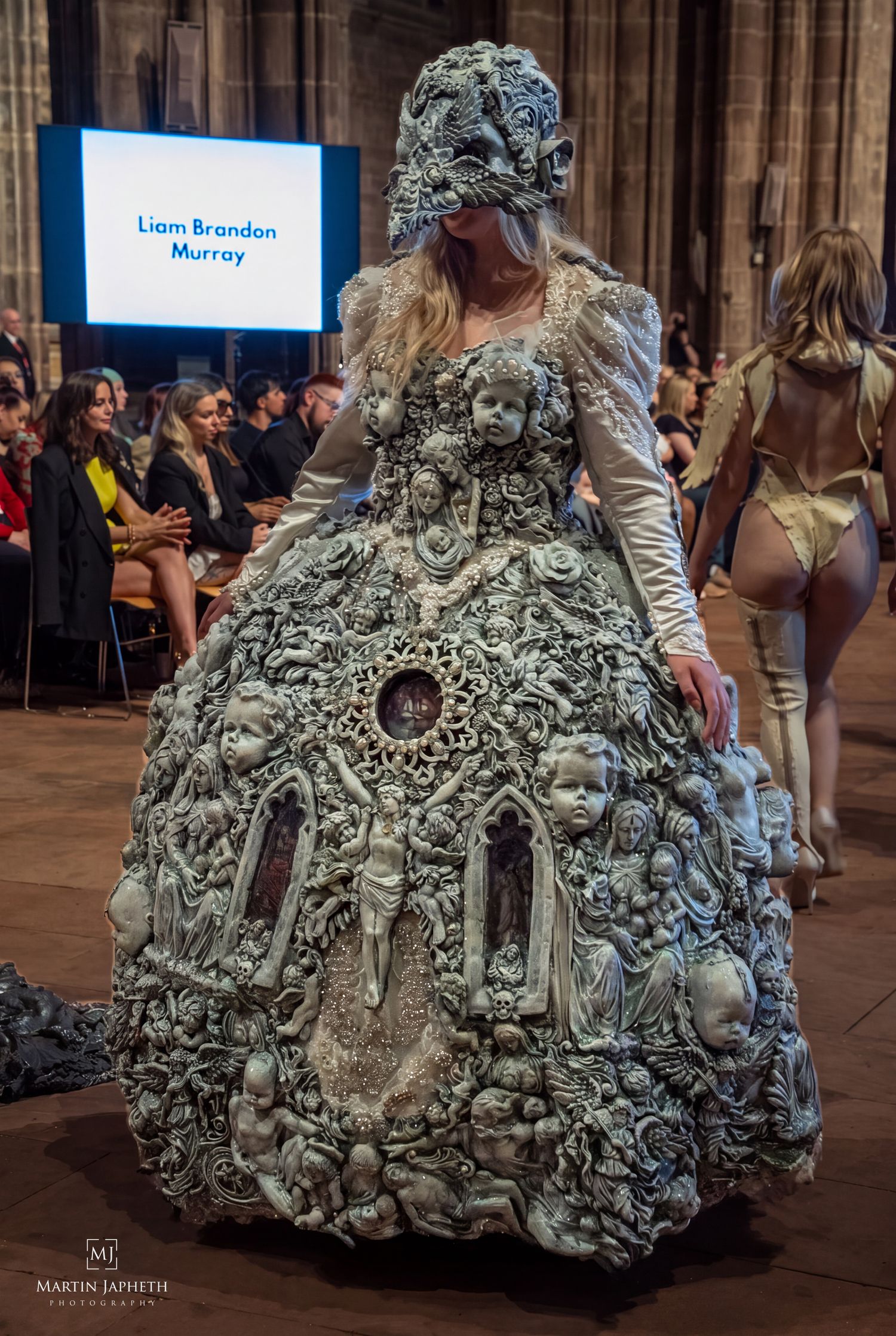 Model wearing an elaborate sculptural gown adorned with cherubs and gothic architecture by Liam Brandon Murray at Cheshire Fashion Week.