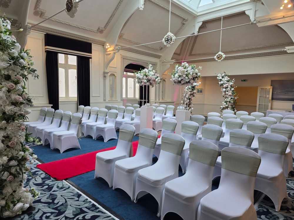 Indoor wedding ceremony venue with white chair covers and red aisle runner in an elegant room with hanging decorations.  St. George's Hotel