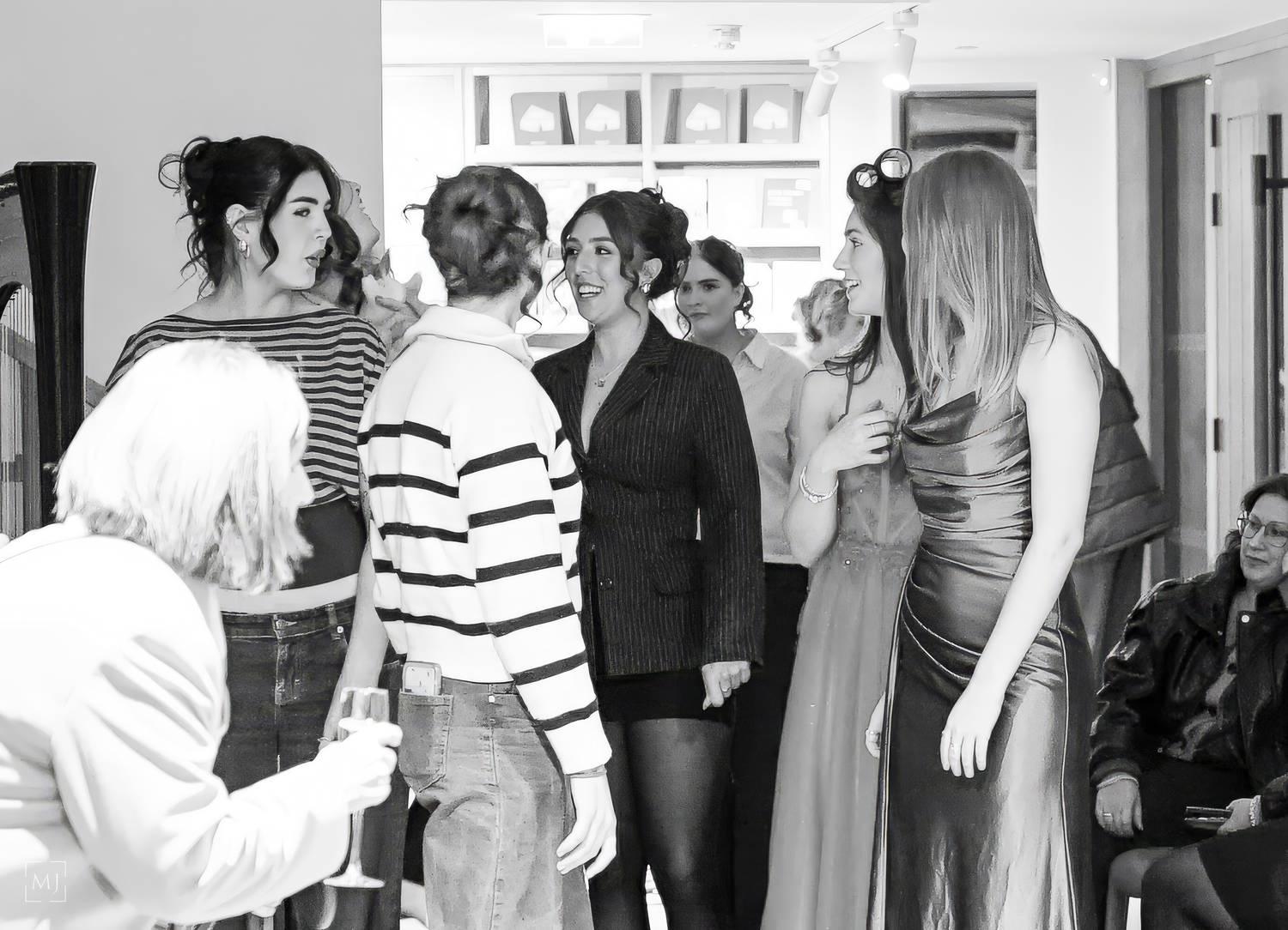 A black and white photograph shows people standing in a crowded hallway or corridor waiting in line.