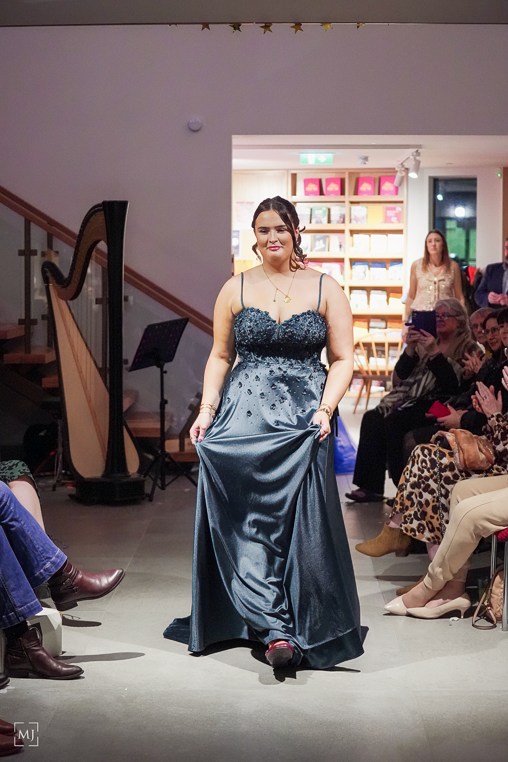 A fashion show sequence featuring a model in a navy blue satin evening gown posing on a runway with audience members visible. Fashion Photo