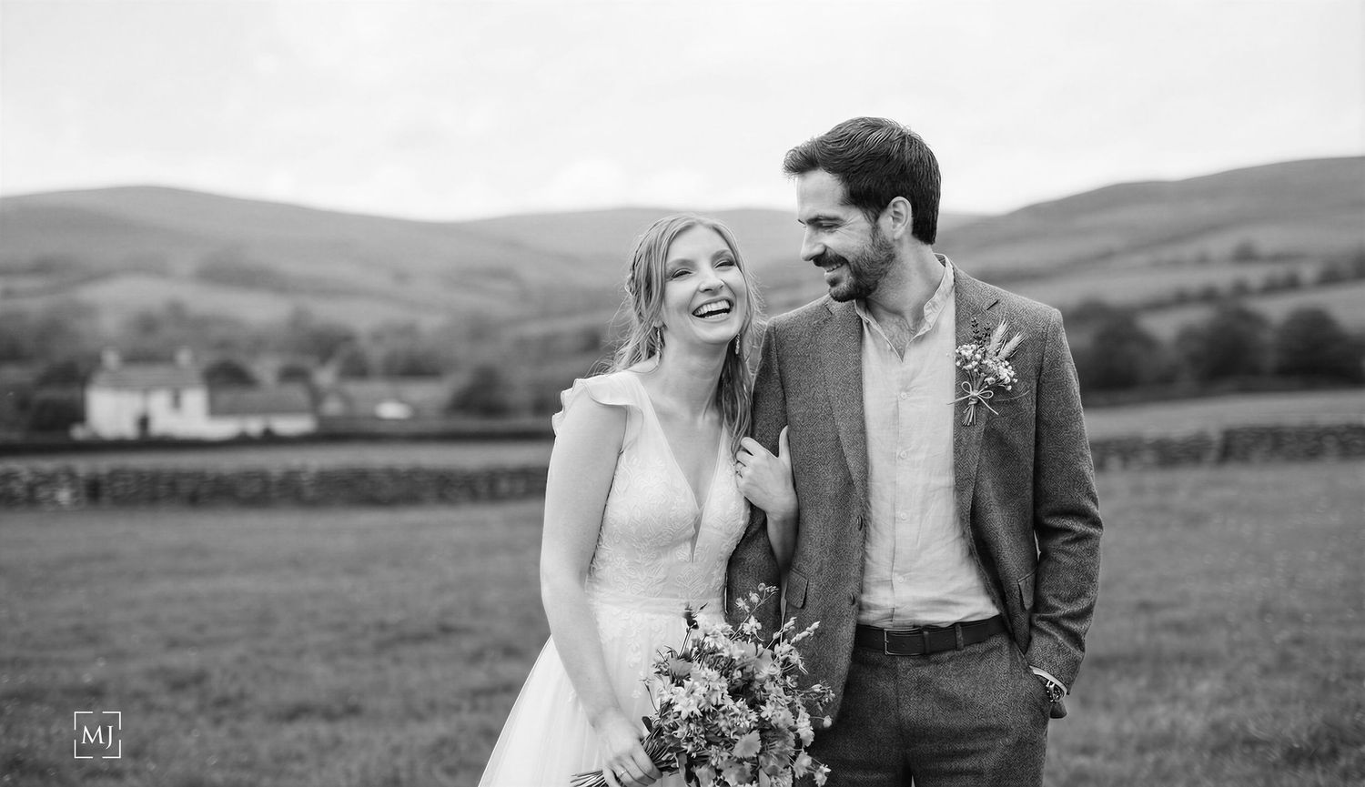 Joyful wedding couple sharing a laugh in a countryside setting with rolling hills. Wedding Photographer Martin Japheth